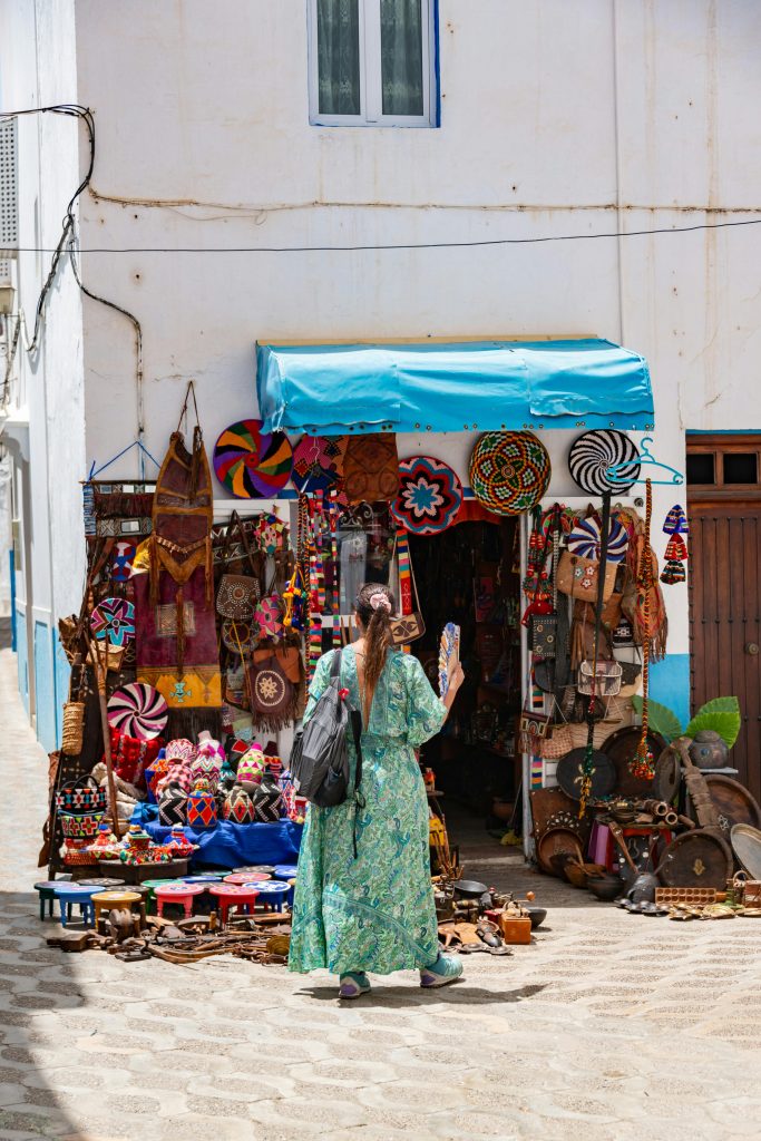 Woman exploring a vibrant market storefront filled with colorful souvenirs on a sunny day.